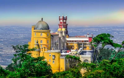 Żółte i czerwone mury Pałacu Pena z kopułą i wieżą zegarową ponad lasem Serra de Sintra