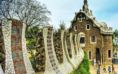 Falisty mur z mozaiki trencadís i pawilon wejściowy w Parku Güell w Barcelonie