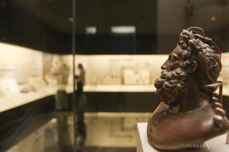 Brązowe popiersie brodatego mężczyzny w wieńcu na tle gablot muzeum
