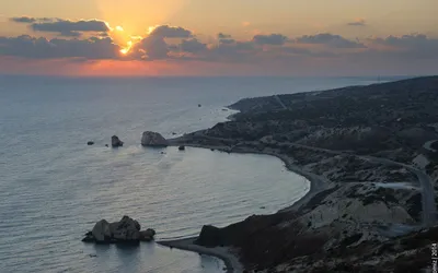 Zachód słońca nad zatoką ze Skałą Afrodyty (Petra tou Romiou) i krętą nadmorską drogą na Cyprze