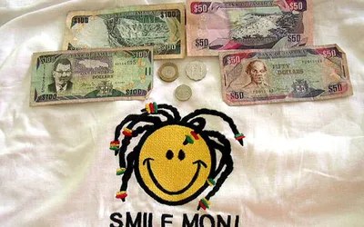 Banknoty 50 i 100 dolarów jamajskich oraz trzy monety na koszulce z napisem Smile Mon