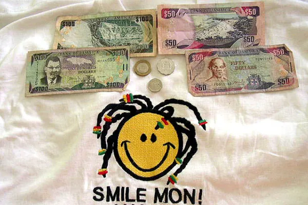 Banknoty 50 i 100 dolarów jamajskich oraz trzy monety na koszulce z napisem Smile Mon