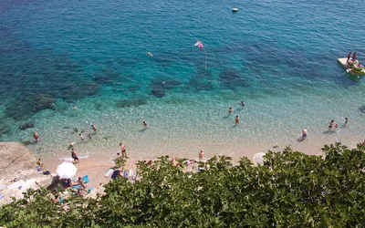 Turkusowa, przejrzysta woda i plażowicze na plaży Banje w Dubrowniku widziani z góry