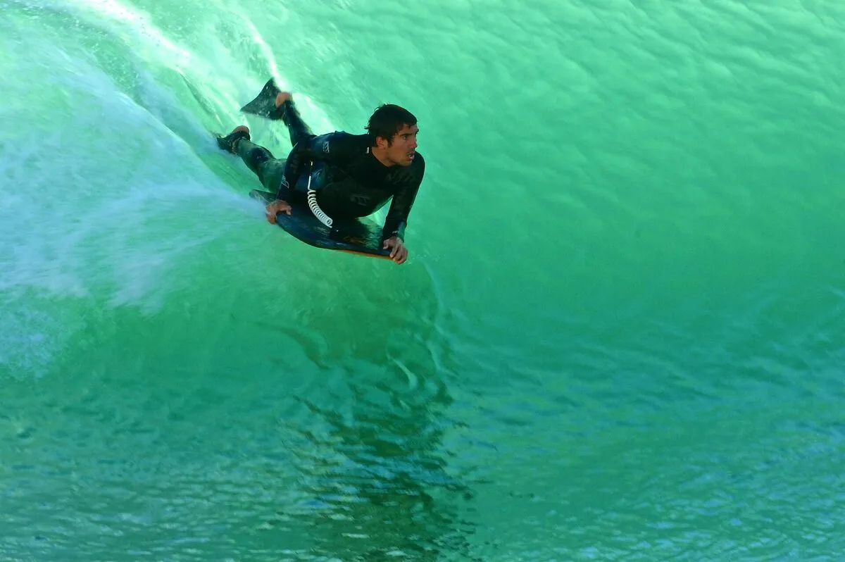 Zawodnik na bodyboardzie w kombinezonie piankowym ślizga się po zielonej ścianie fali