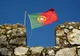 Flaga Portugalii powiewająca nad kamiennymi blankami murów obronnych na tle błękitnego nieba