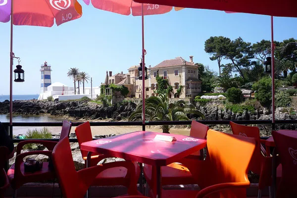 Czerwone stoliki kawiarni nad zatoką w Cascais z widokiem na latarnię Santa Marta