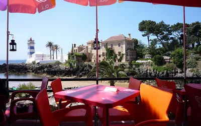 Czerwone stoliki kawiarni nad zatoką w Cascais z widokiem na latarnię Santa Marta