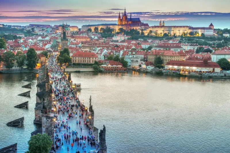 Most Karola pełen ludzi o zmierzchu, a w tle Zamek Praski nad Wełtawą