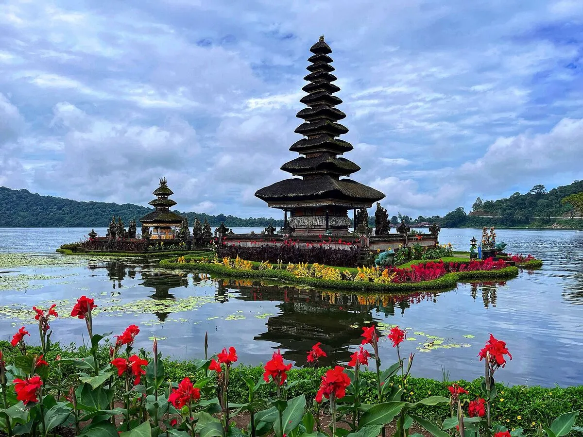 Wielopoziomowa wieża meru świątyni Pura Ulun Danu Bratan na wysepce na jeziorze Bratan na Bali, na pierwszym planie czerwone kwiaty