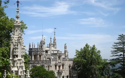 Zdobione wieżyczki pałacu Quinta da Regaleira wśród drzew parku w Sintrze