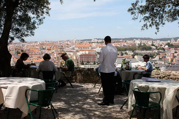 Goście przy stolikach restauracji na tarasie z widokiem na dachy Lizbony