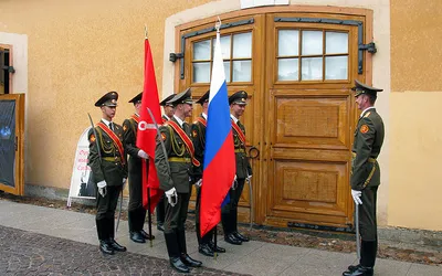 Żołnierze warty honorowej z flagami przed drewnianymi drzwiami w Twierdzy Pietropawłowskiej