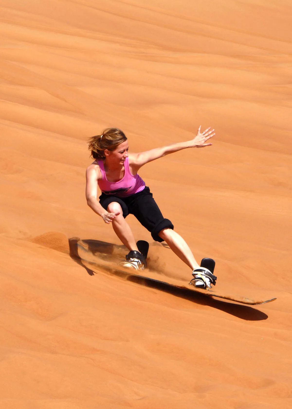 Kobieta zjeżdżająca na desce sandboardowej po zboczu czerwonej wydmy na pustyni pod Dubajem