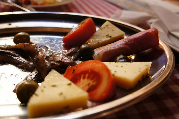Paški ser podany z wędzoną szynką, oliwkami, anchois i pomidorem