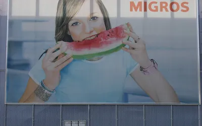 Billboard z logo Migros przedstawiający dziewczynę jedzącą arbuza