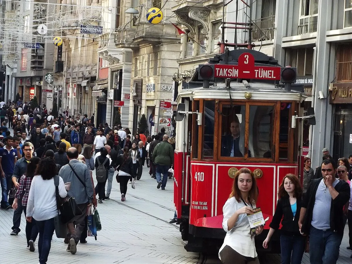 Tłum przechodniów na deptaku İstiklal w Stambule, obok czerwony zabytkowy tramwaj Taksim-Tünel