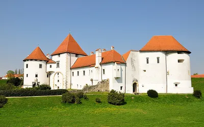 Biała twierdza Stari Grad w Varaždinie z czerwonymi dachami baszt na tle zielonych wałów