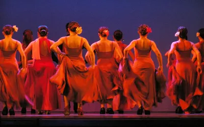 Tancerki flamenco w czerwonych sukniach na scenie, widziane od tyłu