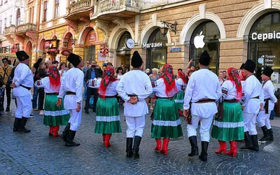 Pary tancerzy w ukraińskich strojach ludowych – białe koszule, zielone spódnice i czerwone buty – tańczą na ulicy w Czerniowcach