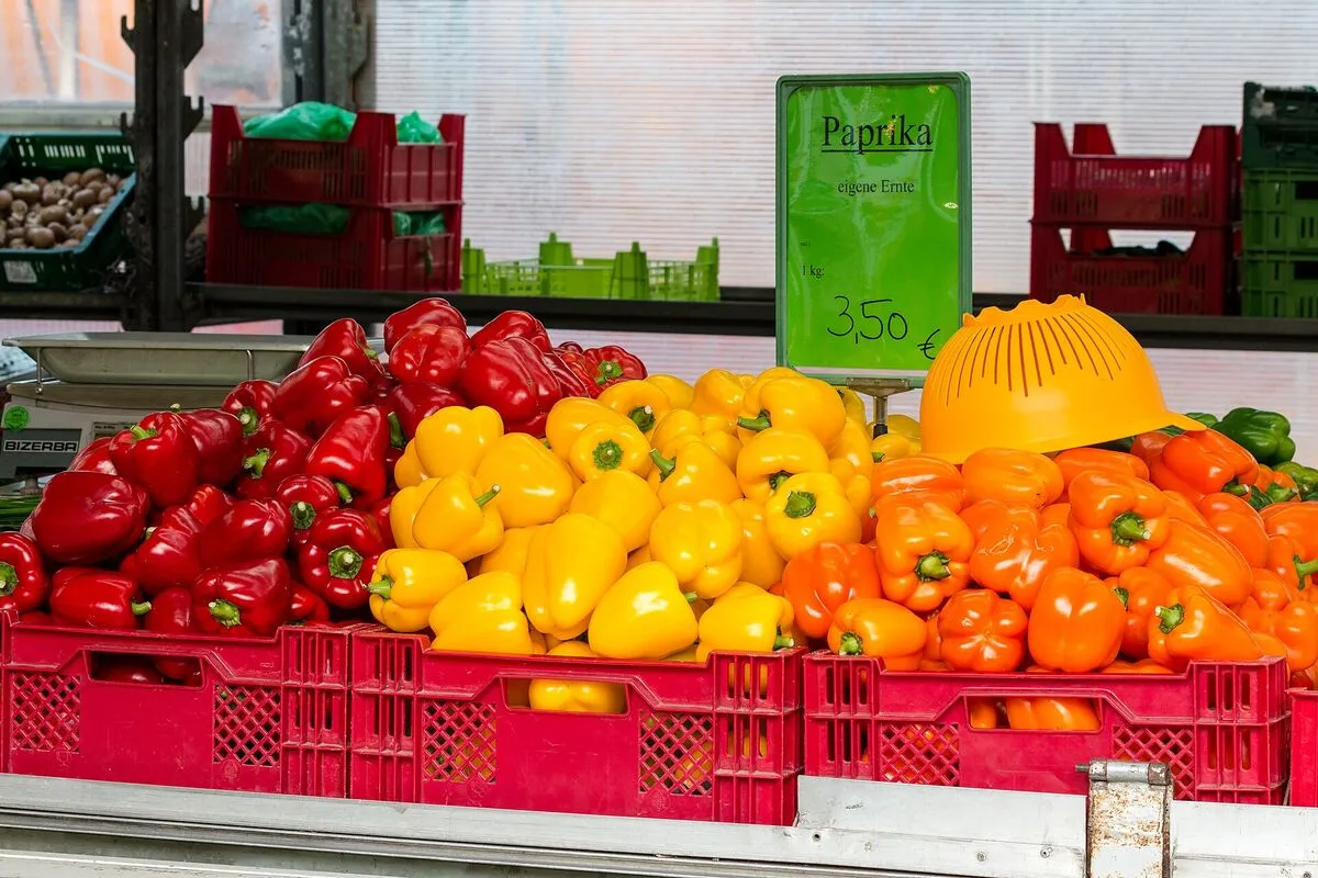 Czerwona, żółta i pomarańczowa papryka w skrzynkach na straganie, obok tabliczka z ceną 3,50 € za kilogram