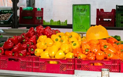 Czerwona, żółta i pomarańczowa papryka w skrzynkach na straganie, obok tabliczka z ceną 3,50 € za kilogram