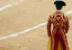 Torero w czerwono-złotym stroju z płachtą stoi tyłem na piaszczystej arenie