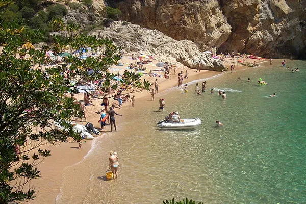 Plażowicze na piaszczystej plaży w zatoce otoczonej skałami
