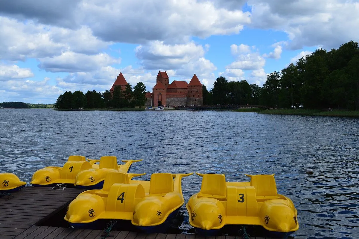 Żółte rowery wodne przy pomoście nad jeziorem Galwe, w tle zamek w Trokach