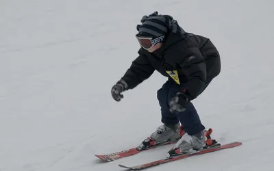Dziecko w goglach zjeżdża na nartach po ośnieżonym stoku w górach Troodos