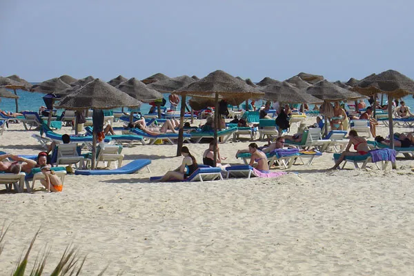 Turyści wypoczywający na leżakach pod słomianymi parasolami na plaży w Tunezji