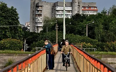 Mieszkańcy ukraińskiego miasta na kładce z czerwonymi barierkami, w tle blok