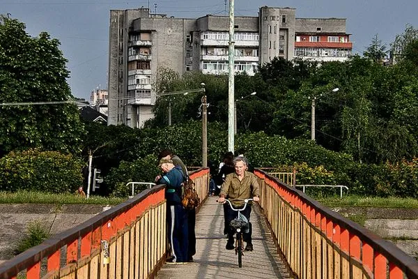 Mieszkańcy ukraińskiego miasta na kładce z czerwonymi barierkami, w tle blok