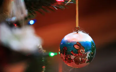 Malowana bombka z zajączkiem zawieszona na choince z kolorowymi lampkami