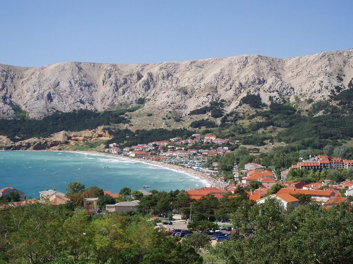 Zatoka w Bašce z długą żwirową plażą Vela, czerwonymi dachami miasteczka i skalistymi górami w tle