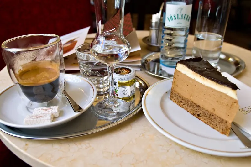 Kawa, szklanka wody i kawałek tortu na marmurowym stoliku wiedeńskiej Café Museum