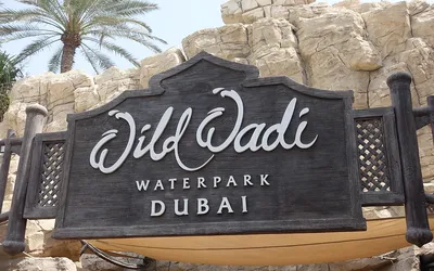 Drewniany szyld z napisem Wild Wadi Waterpark Dubai na tle sztucznych skał