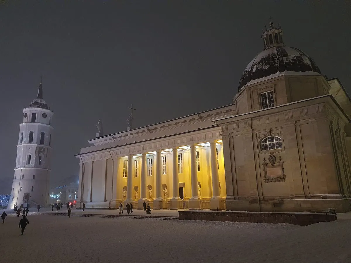 Oświetlona po zmroku Katedra Wileńska i dzwonnica, na placu zalega śnieg