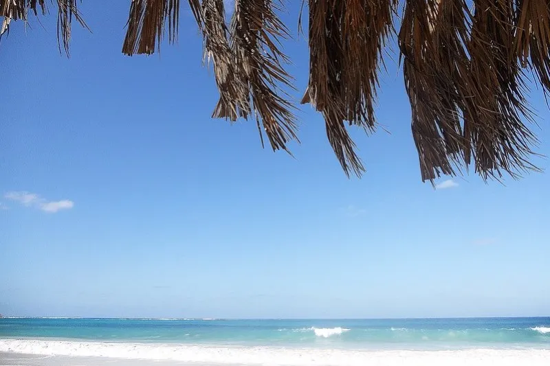 Biała plaża i turkusowe morze widziane spod strzechy parasola z liści palmowych