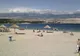 Plażowicze pod słomianymi parasolami na jasnej żwirowej plaży Zrće, w tle pasmo Velebitu
